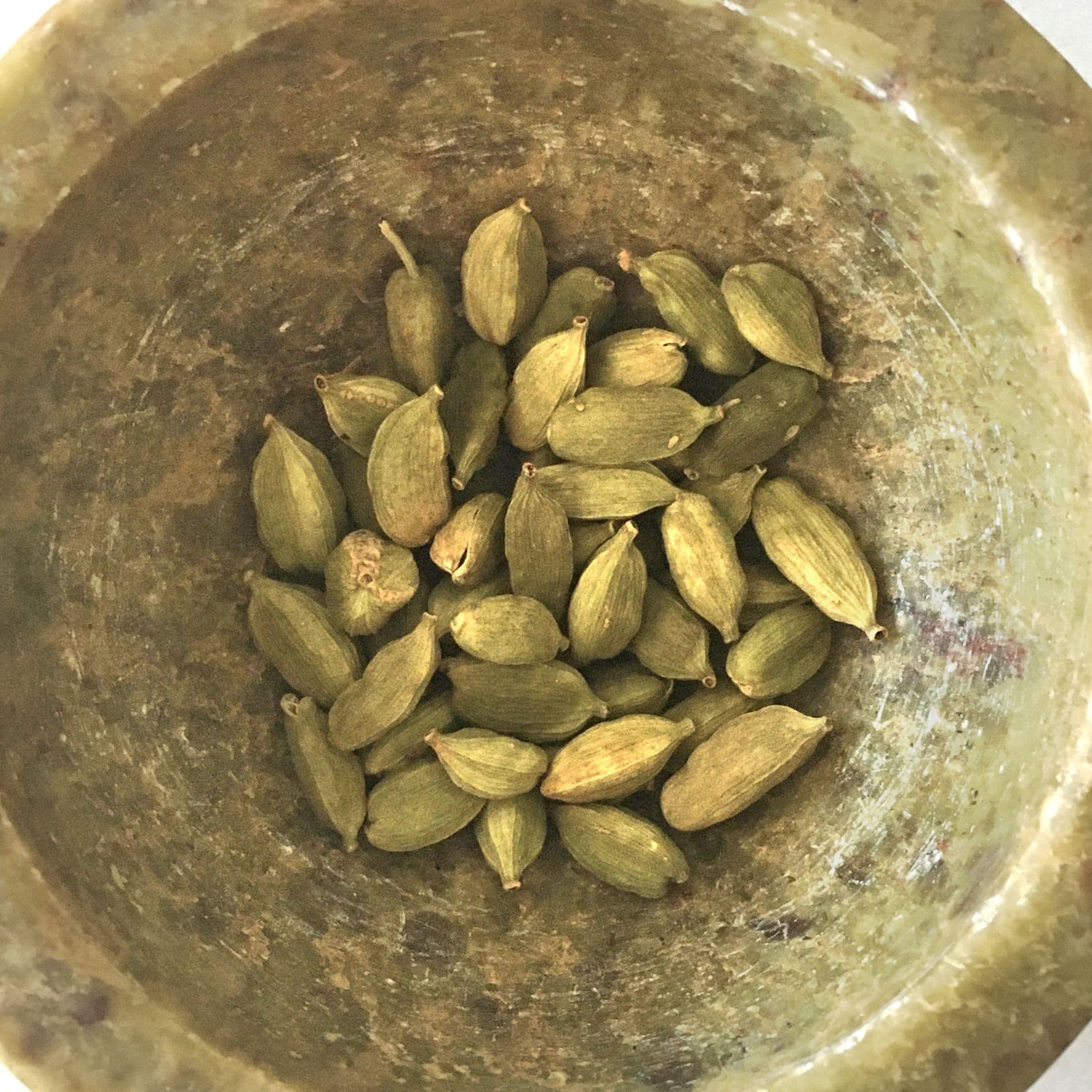Green cardamom pods in a brass bowl