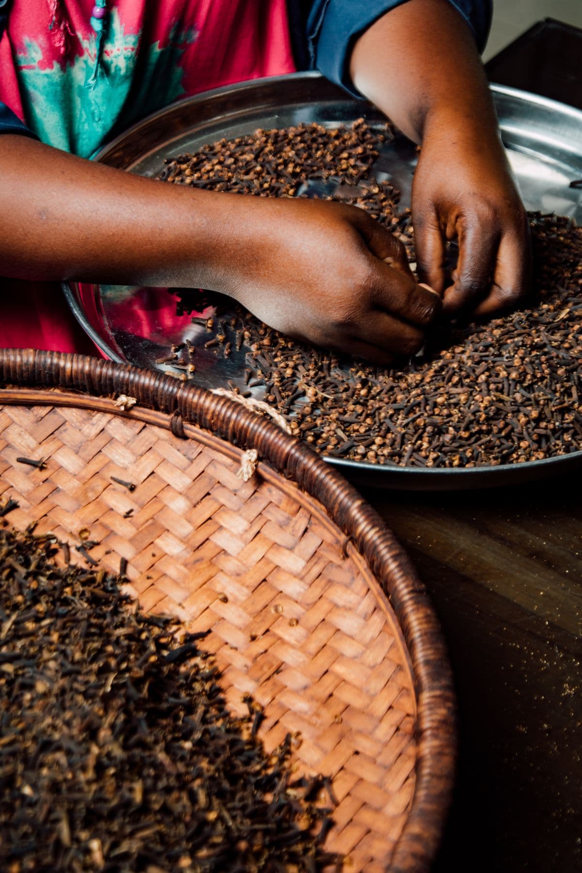 Hands sorting dried spices over a woven basket